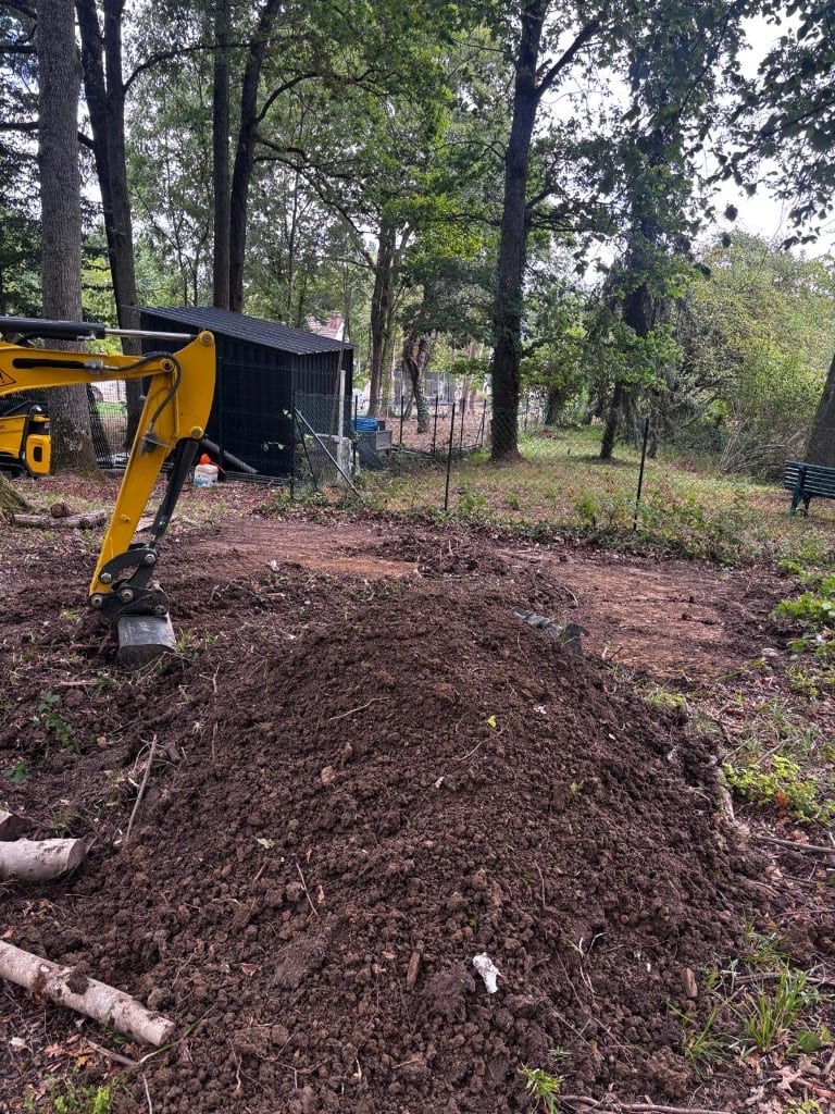 Terrassement au godet : tas de terre et mini-pelle en fond de jardin